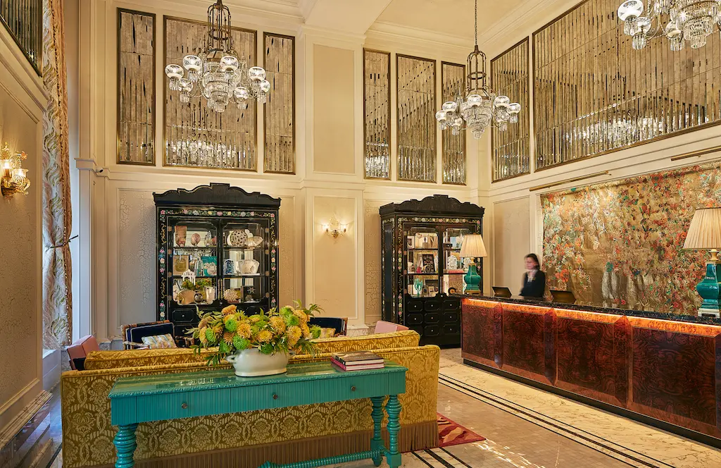 Beautifully arranged lobby with a lady behind the counter and three chandeliers glowing.