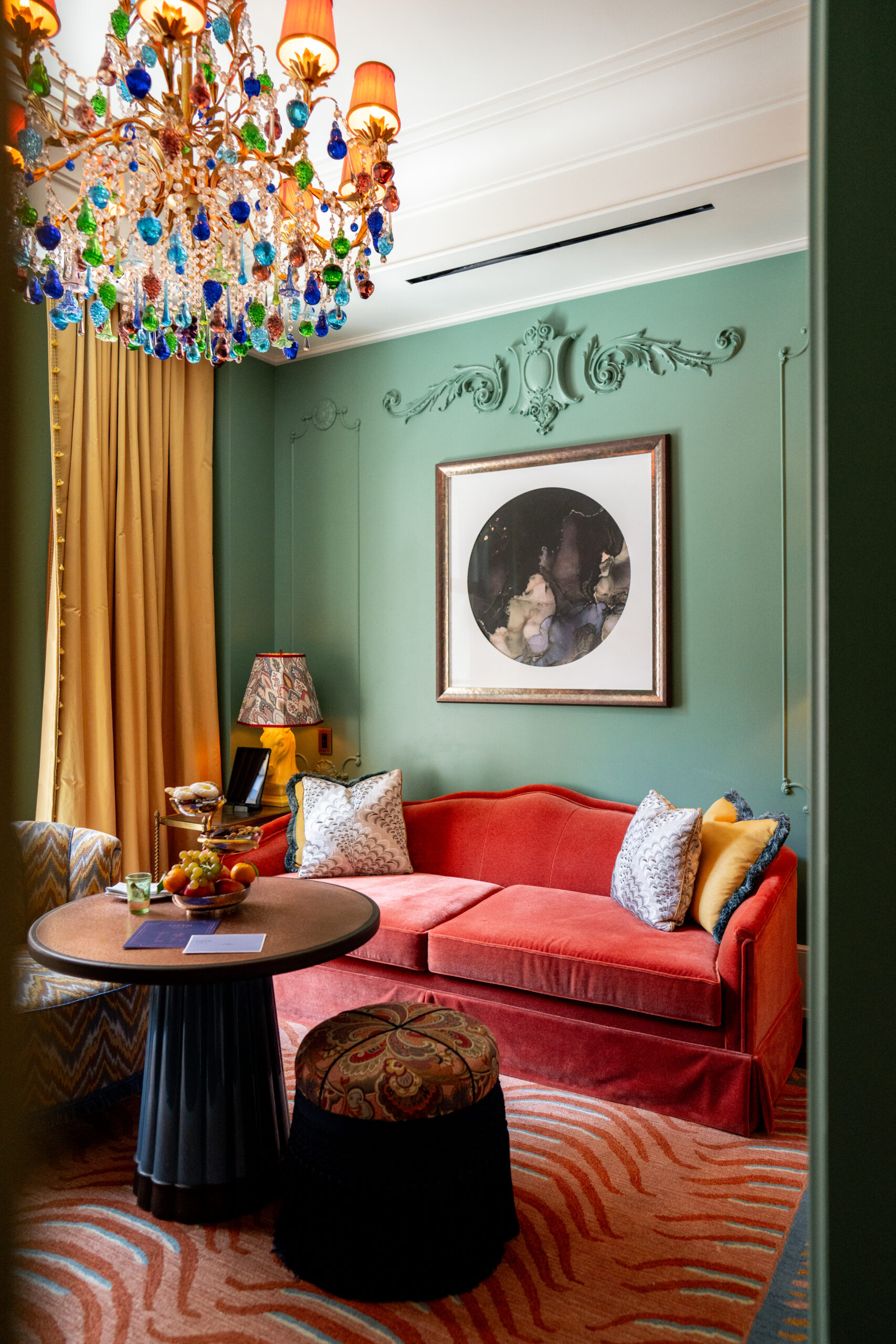 A well-arranged sofa set with a coffee table near the window and a colorful chandelier hanging above.