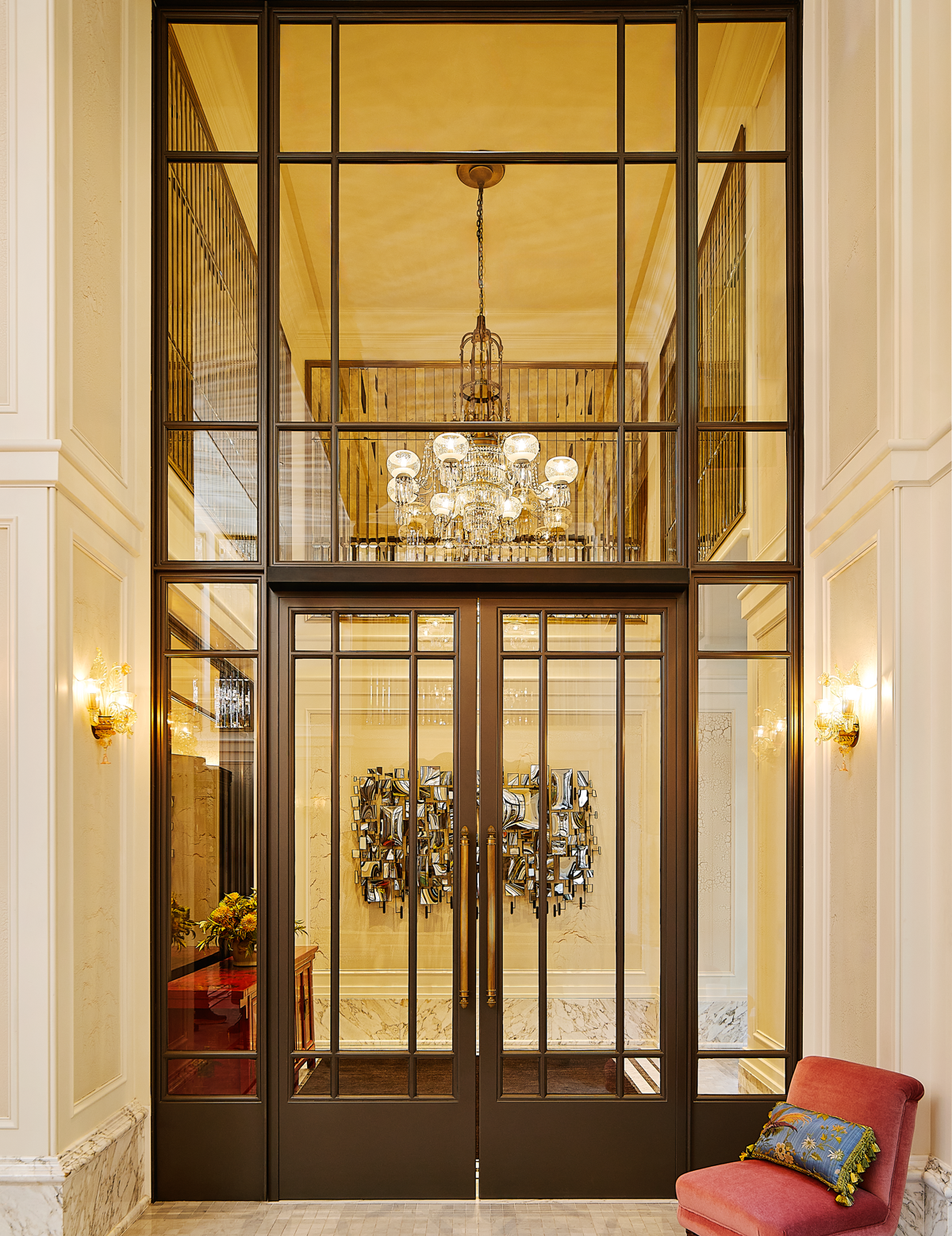 A beautiful glowing chandelier hangs at the entrance of The Fifth Ave Hotel.