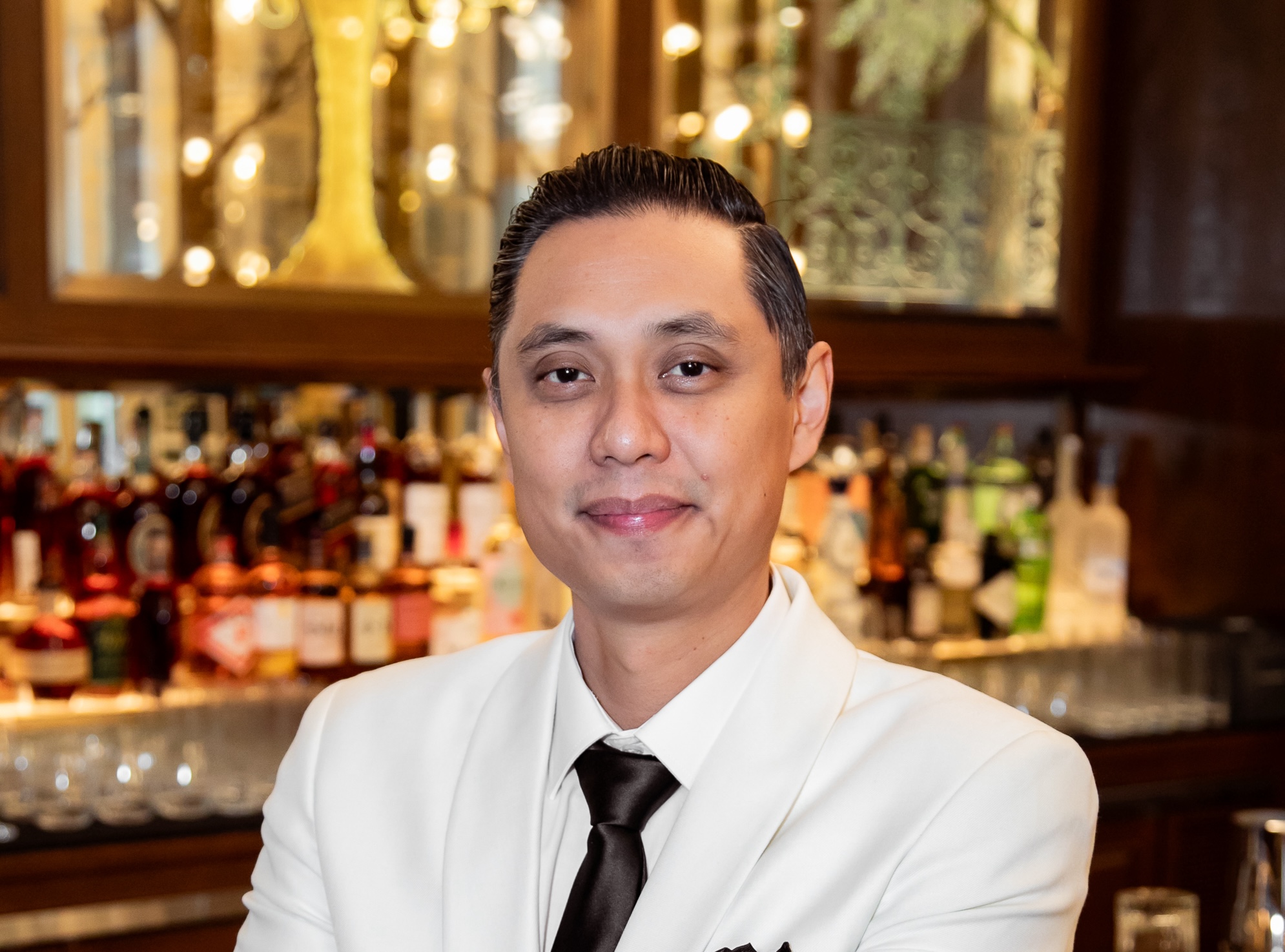 A man in a white suit stands beside the bar counter.