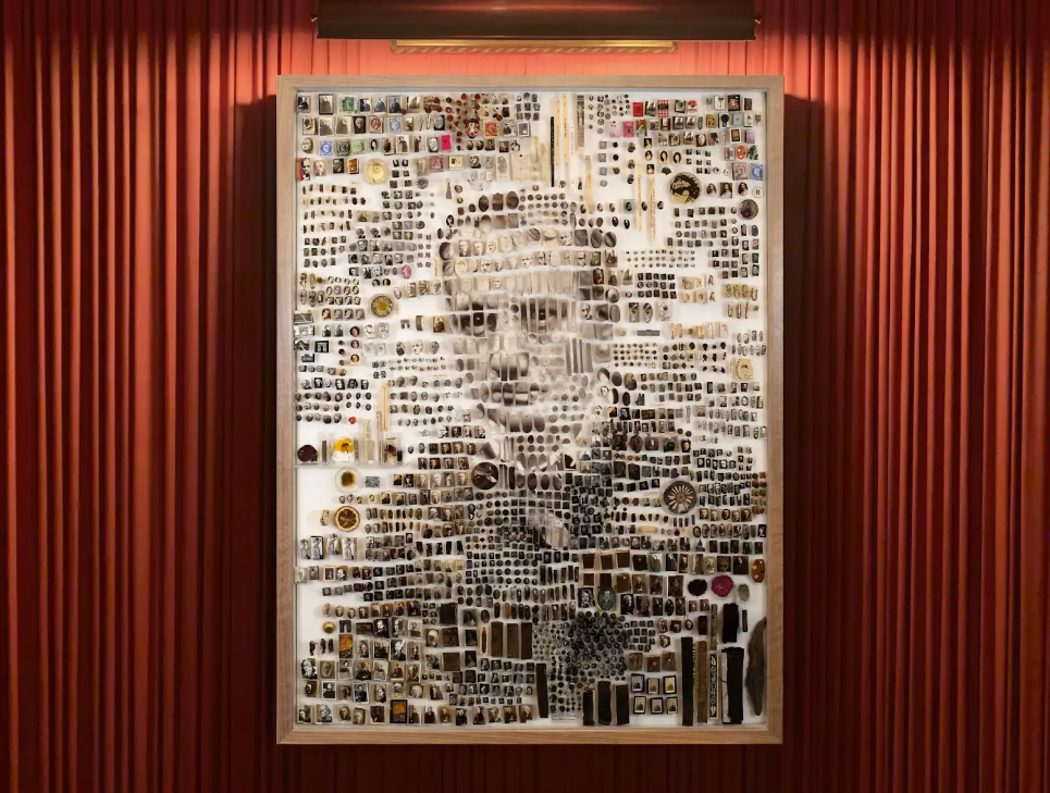 A mosaic portrait made from various small objects, including trinkets, photographs, and memorabilia, displayed against a red backdrop.