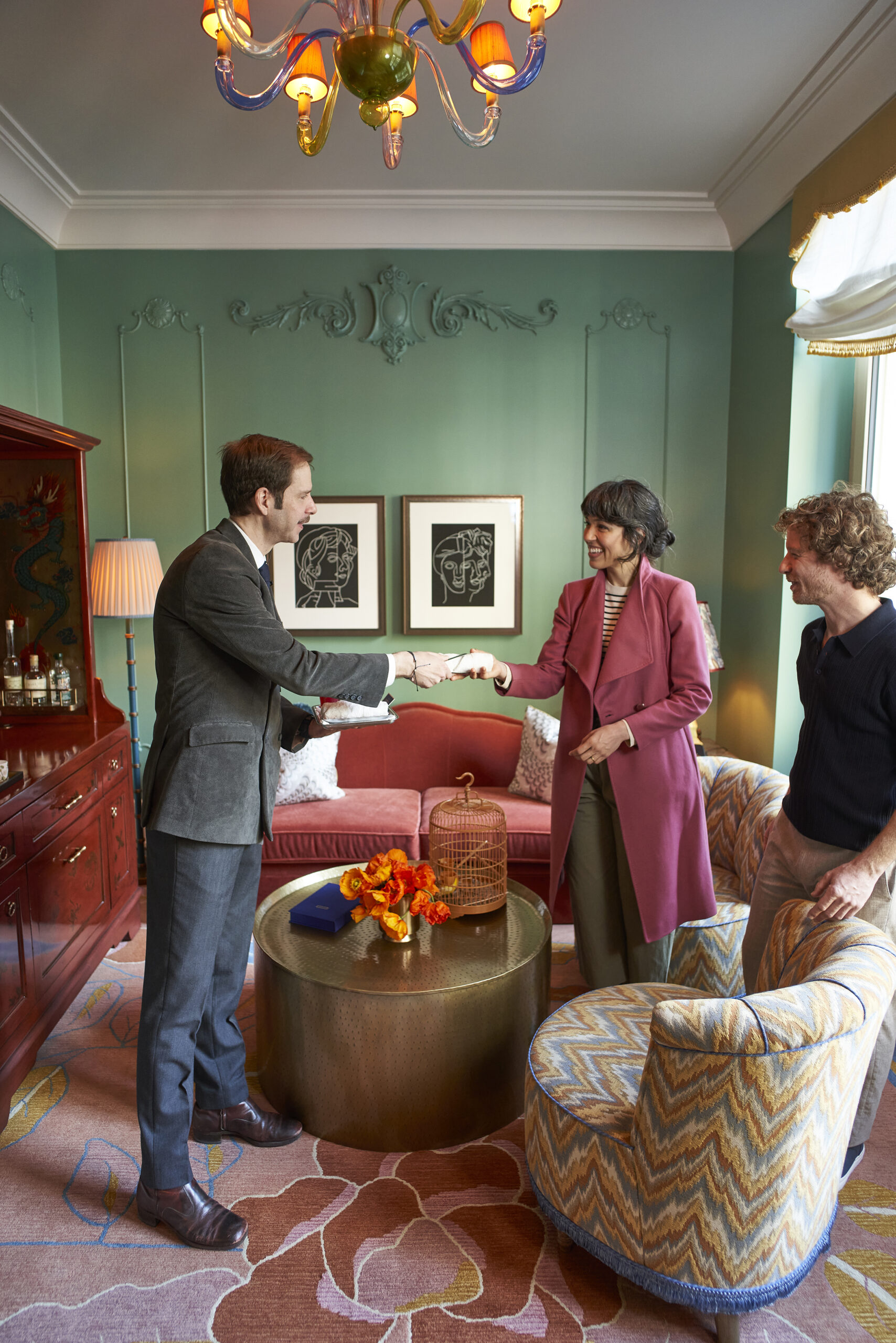 Two people smile while exchanging an item in a stylishly decorated room with green walls and modern art.