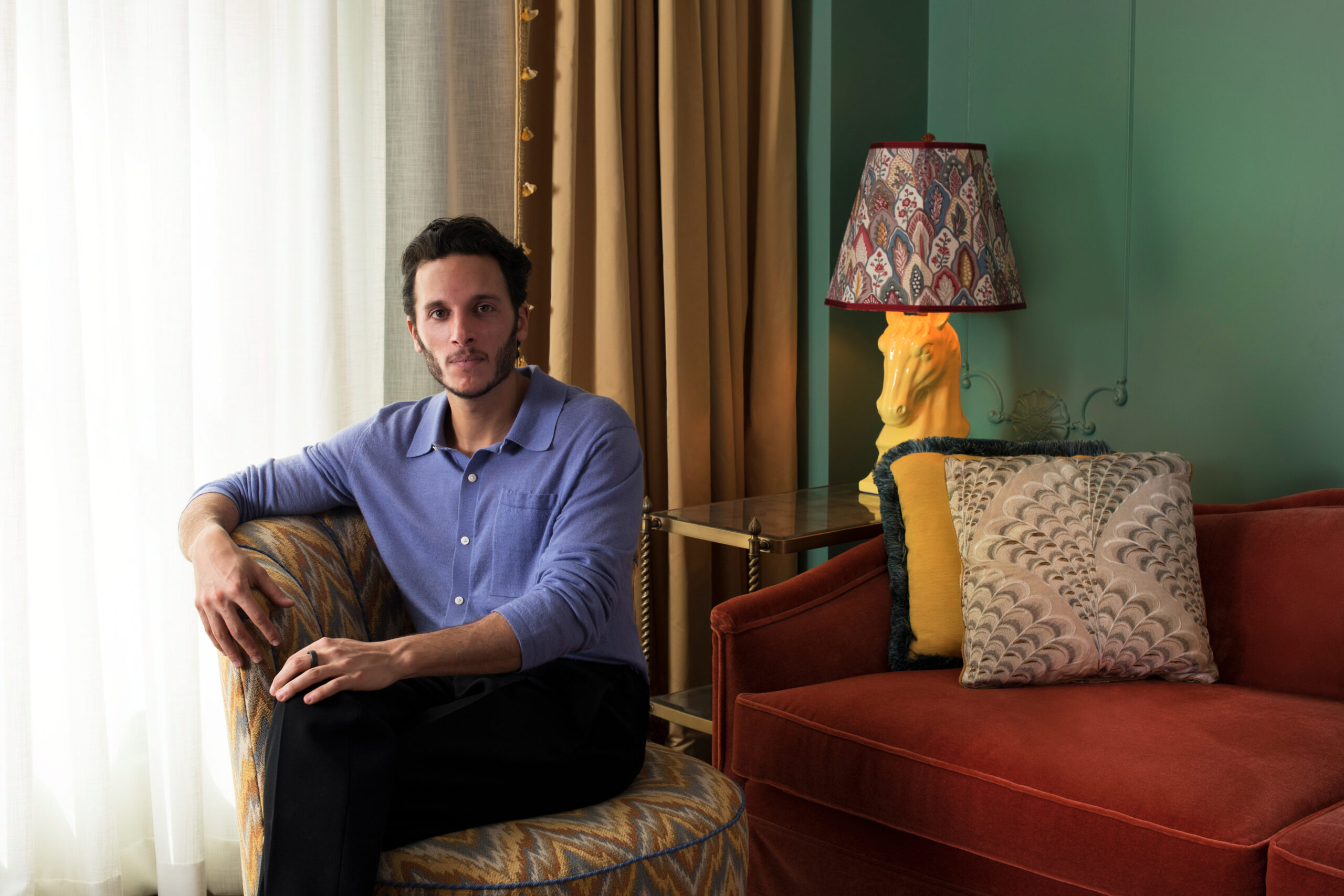 Man sitting on a patterned chair in a warmly decorated room